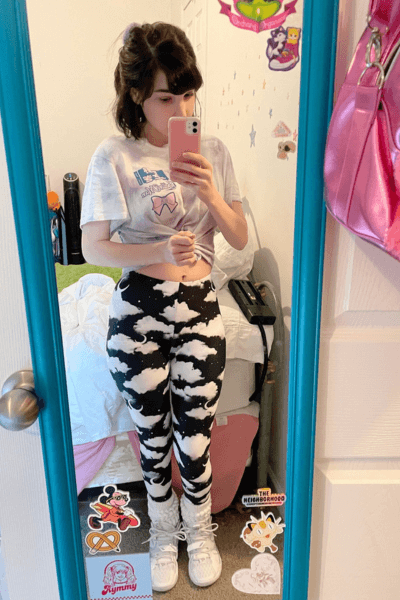 Casual outfit selfie in mirror, featuring a cropped tee and cloud-patterned leggings, with colorful room decor.